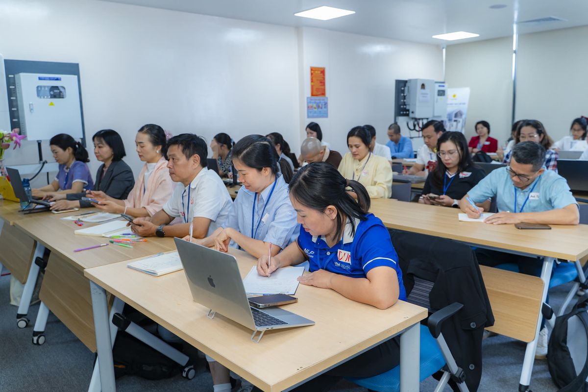 Học viên ngồi theo dãy bàn, người ghi chép vào sổ, người thao tác trên laptop và điện thoại