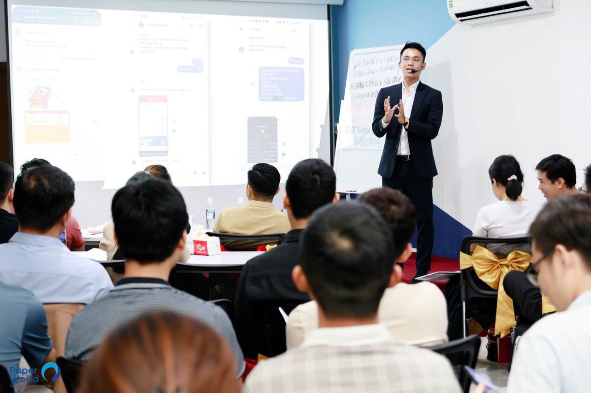 Lê Văn Cương đứng giảng trong một lớp học nhỏ, phía sau là màn chiếu
